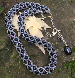 This fancy Black and Multi Iridescent Netted Treasure Necklace is held together by crystal and iridescent seed beads, which give it a subtle flash. The tail ends with three Swarovski crystals and a smooth black oval bead. This necklace is adjustable and can be worn from 20 1/2" to 23".  