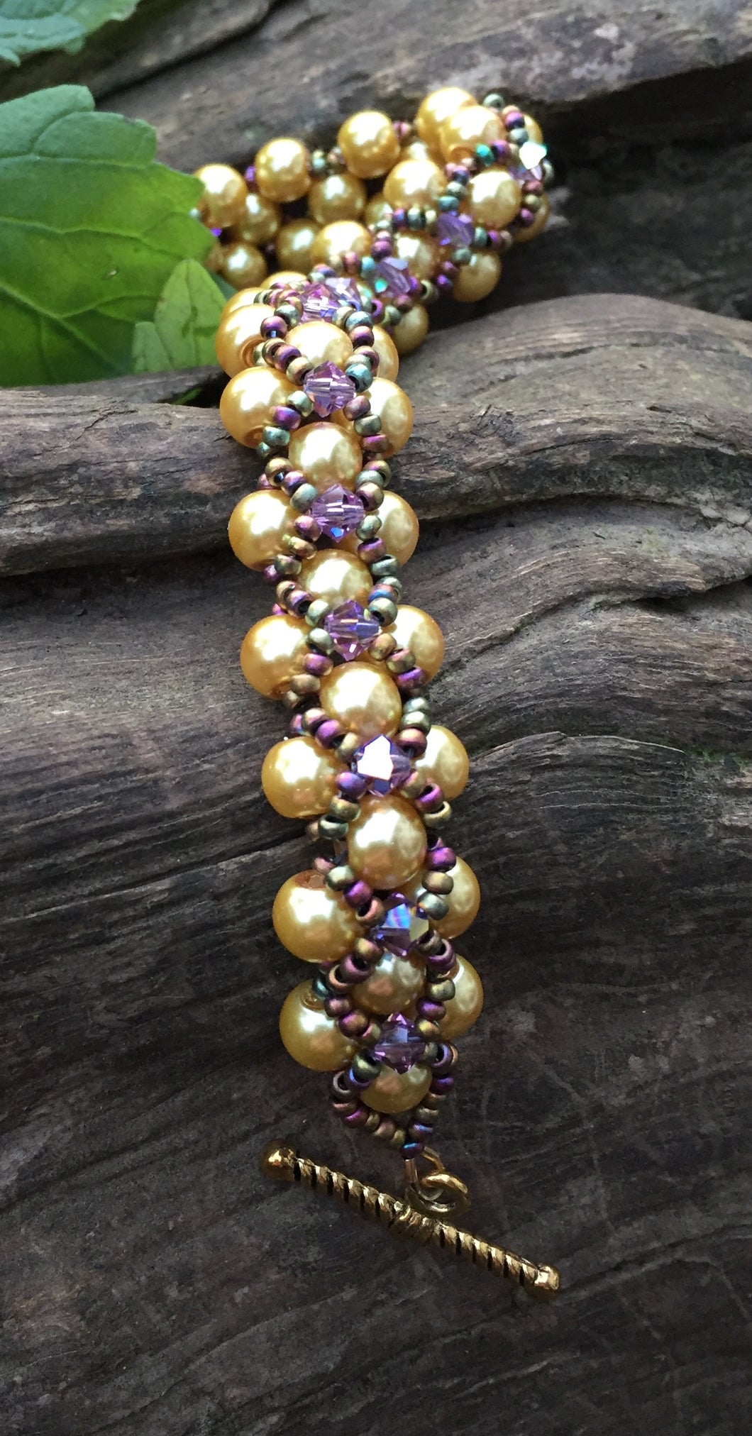 This Golden glass pearl and Amethyst bicone Swarovski crystal bracelet is netted together with Matte Iris seed beads and measures 7 7/8