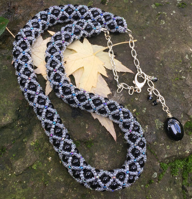 This fancy Black and Multi Iridescent Netted Treasure Necklace is held together by crystal and iridescent seed beads, which give it a subtle flash. The tail ends with three Swarovski crystals and a smooth black oval bead. This necklace is adjustable and can be worn from 20 1/2