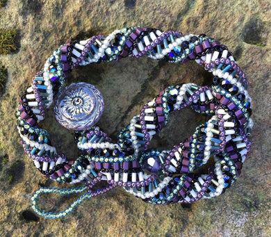 This meticulously woven helix necklace consists of Czech Glass beads in purple, black, green and cream and it ends with an iridescent Czech glass button clasp.  It is adjustable and can be worn between 15