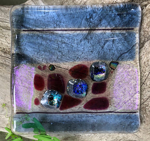 This transparent and Dichroic fused glass dish has the charm of both stripes and speckles! While flat in design, the surface is bubbly, making it a great option for holding jewelry or incense. This dish measures almost 4" x 4".