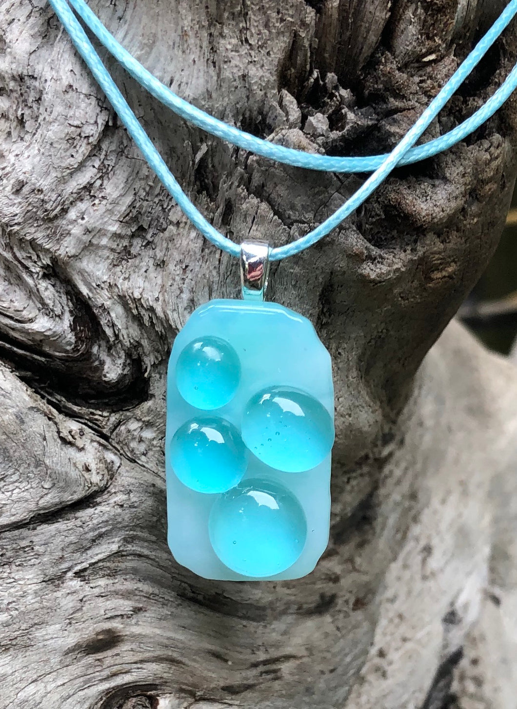 The Bubblicious Aqua Bubbles Fused Glass Pendant measures approximately 1 1/2” x 3/4” on floats on a waxed Irish cotton cord which is adjustable from 17 1/2” to 19 1/4”.