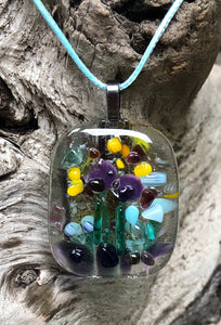 So much activity on this fused glass pendant, could be pollinators, butterflies, birds... this pendant with Purples, Aquas, Yellows and Greens measures 1 5/8” by 1 3/8”. The light blue waxed Irish cotton cord is adjustable from 17 3/4” to 19 3/4”.