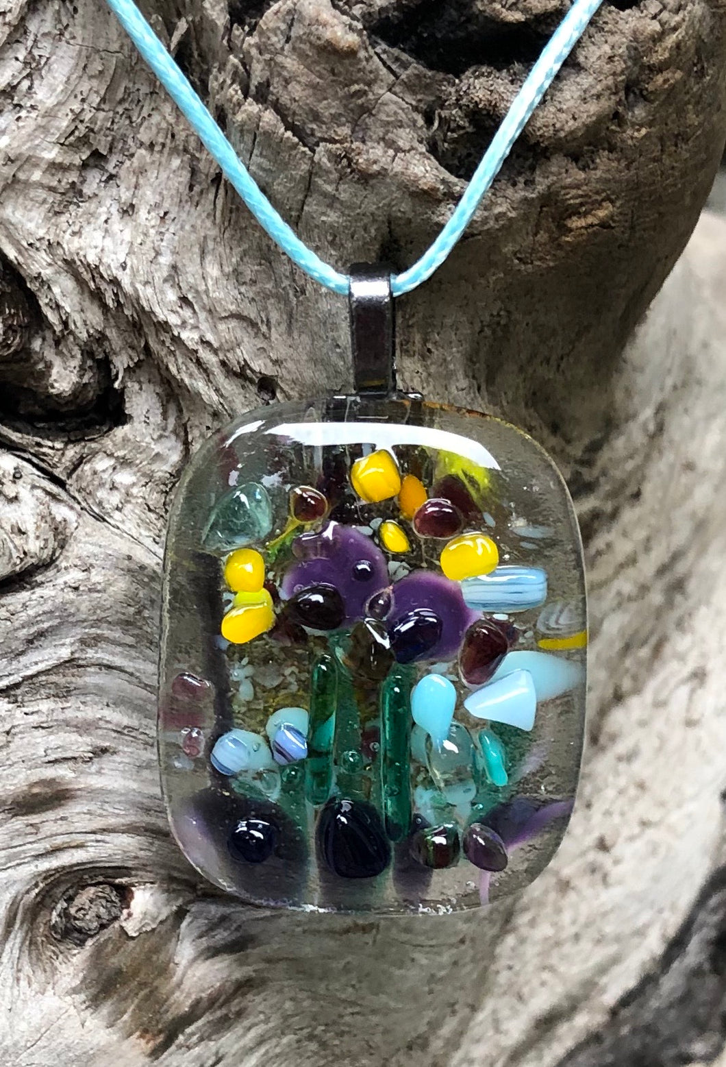 So much activity on this fused glass pendant, could be pollinators, butterflies, birds... this pendant with Purples, Aquas, Yellows and Greens measures 1 5/8” by 1 3/8”. The light blue waxed Irish cotton cord is adjustable from 17 3/4” to 19 3/4”.