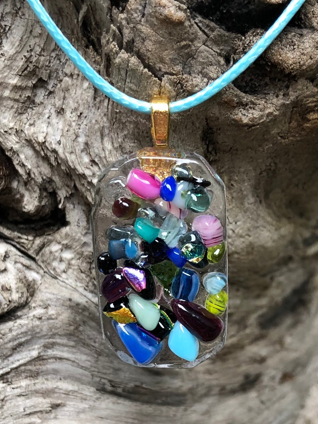 This colorful fused glass pendant of the Pixie Dust Collection is 1 1/4” by 3/4” and the light blue waxed Irish cotton cord is adjustable from 18” to 19 3/4”. Elements include dichroic glass!